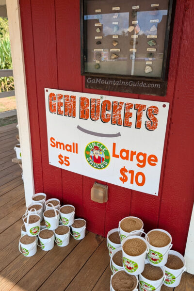 Small and large gem-mining buckets beneath a price sign and gem identification board at Uncle Shuck’s in Dawsonville