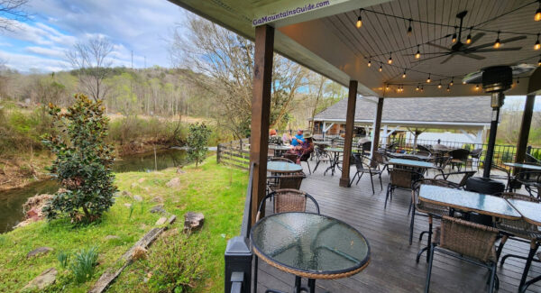 Covered deck with tables and string lights beside the creek at Accent Cellars